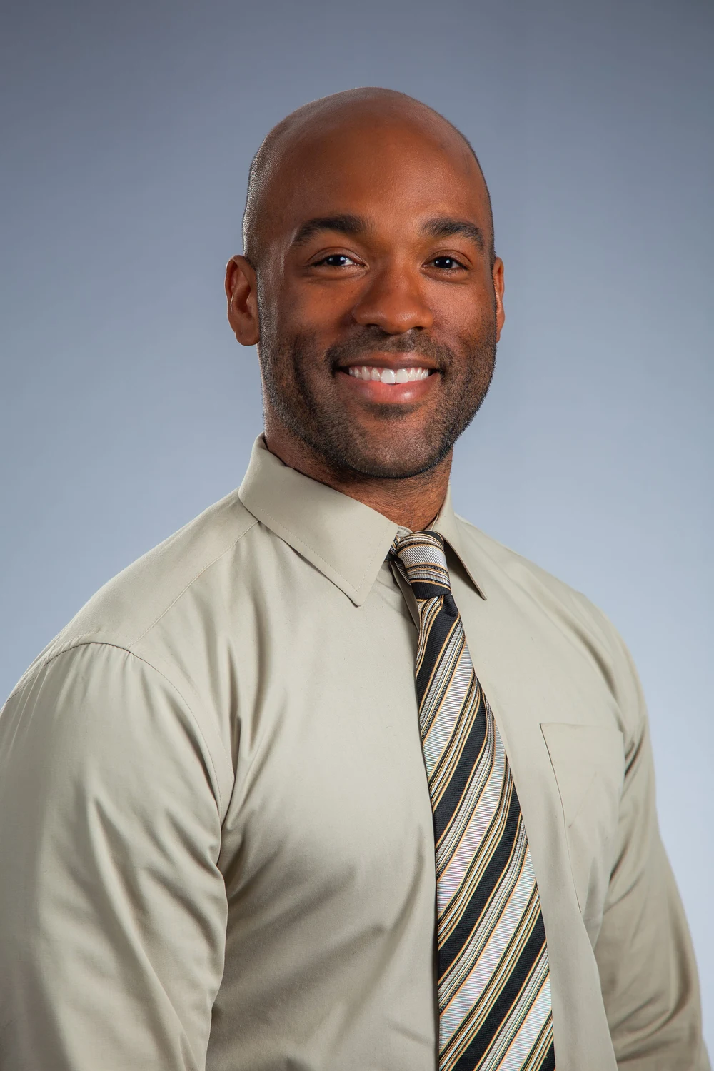 Tyler Allen in a light shirt and striped tie, photographed against a gray background.